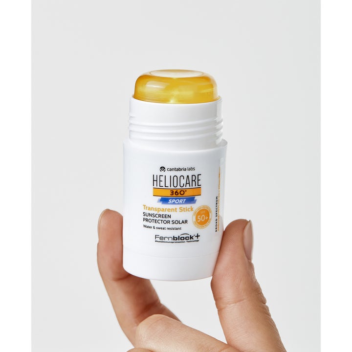 Heliocare Sport Stick SPF 50+ 25 g solbeskyttelse i hvit stift med transparent oransje kjerne holdt av en hånd.