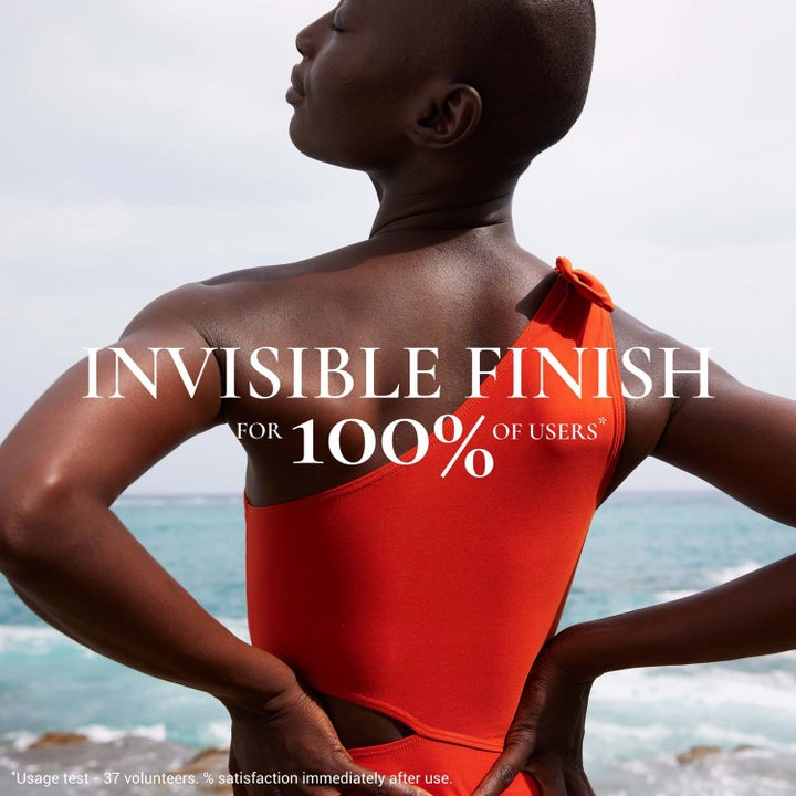 Nuxe Sun Mist Fresh SPF 30 150 ml solkrem til kropp gir usynlig finish vist pÄ kvinne i orange badedrakt ved havet.