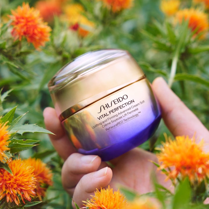 Shiseido Vital Perfection Advanced Soft Cream 50 ml oppstrammende ansiktskrem i gull og lilla krukke blant oransje blomster