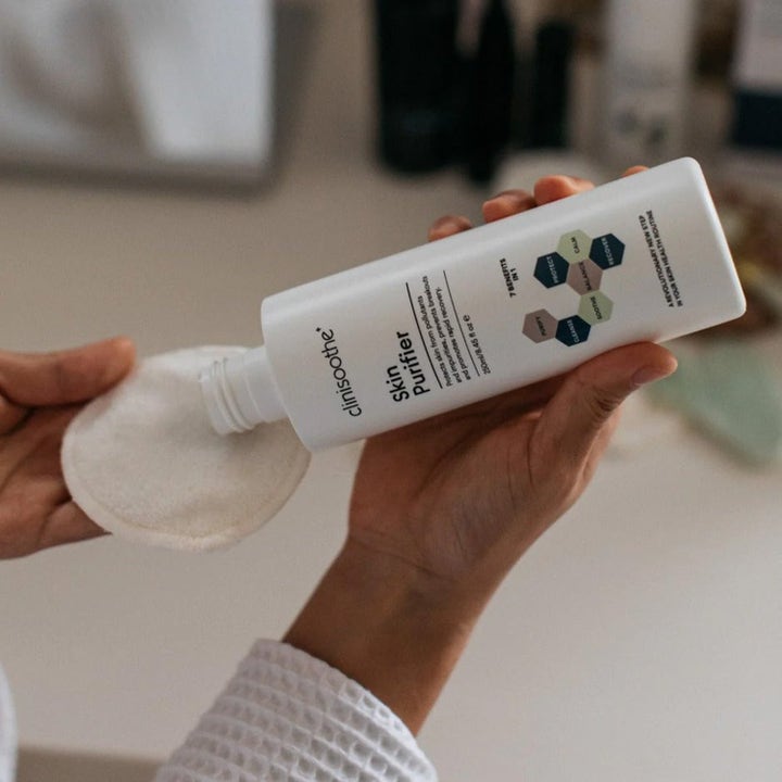 Clinisoothe Skin Purifier 250 ml toner helles på en bomullspad fra en hvit flaske for å rense og berolige huden.