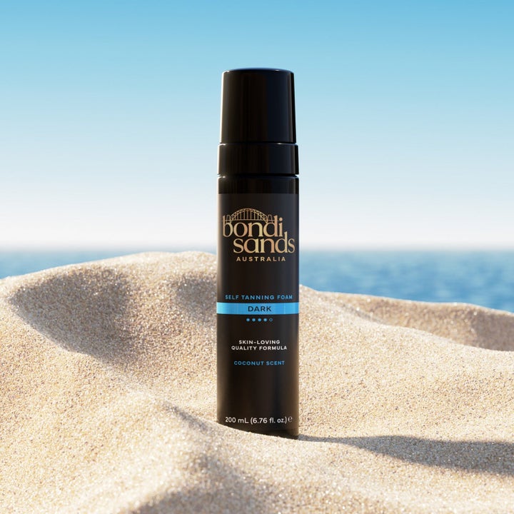 Bondi Sands Self Tanning Foam Dark 200 ml gir dyp brunfarge i svart pumpeflaske plassert på en solfylt sandstrand