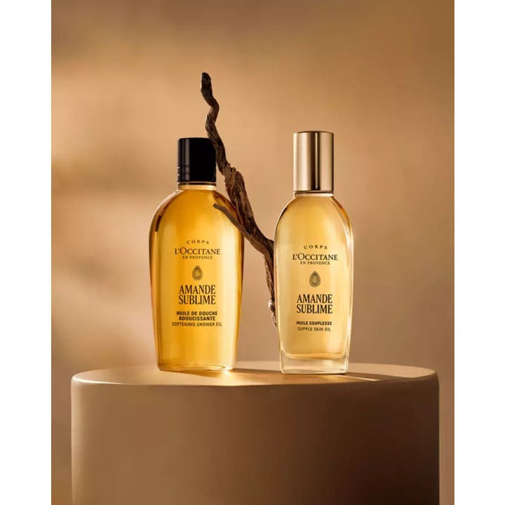 L'Occitane Almond Shower Oil 250 ml mykgjørende dusjolje i en stemningsfull setting med en gren og varmt lys
