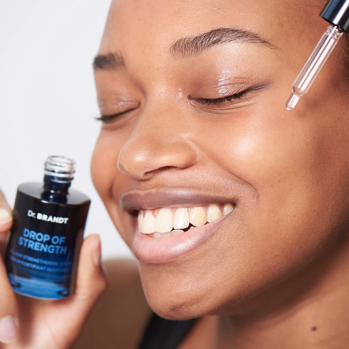 Dr Brandt Drop Of Strength 30 ml styrkende serum i blå glassflaske påføres med pipette på smilende kvinne