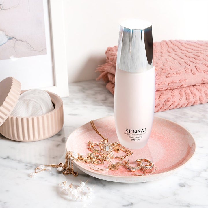 Sensai Cellular Performance Emulsion II fuktighetsgivende hudpleie i hvit flaske på et rosa fat med gullsmykker