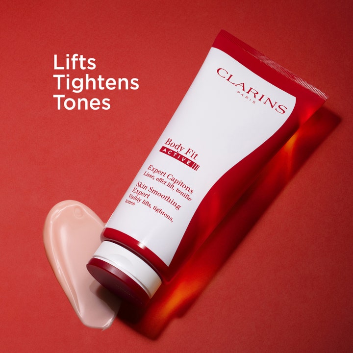 Clarins Body Fit Active 200 ml strammer opp huden, vist med lys rosa tekstur og rød tube på rød bakgrunn.
