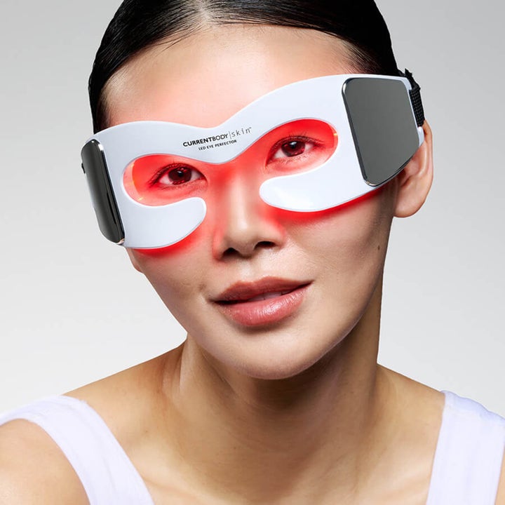 Currentbody Skin LED Eye Perfector hvit øyemaske med rødt lys som behandler huden rundt øynene på en kvinne.