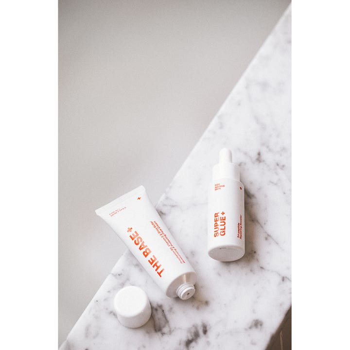 Swiss Clinic Super Glue+ 30 ml reparerende serum for aldrende hud i hvit pipetteflaske på marmoroverflate.