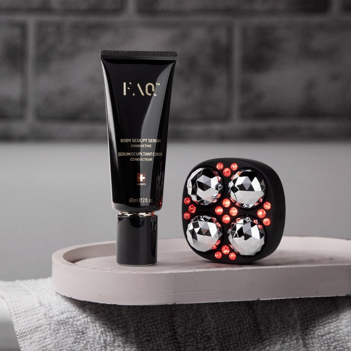 FAQ Swiss FAQ Body Sculpt Serum 60 ml oppstrammende kroppsserum i svart tube ved siden av rødlysenhet på et fat
