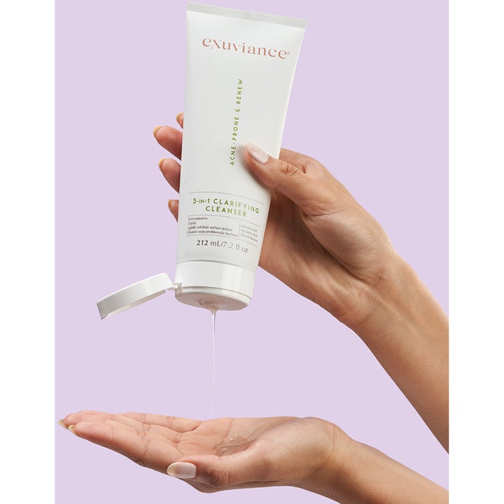 Exuviance 3-in-1 Clarifying Cleanser 212 ml ansiktsrens i hvit tube som helles i en hånd mot lilla bakgrunn