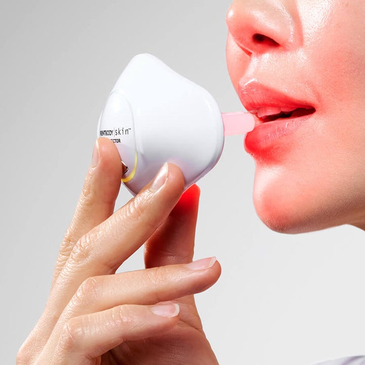 Currentbody Skin LED Lip Perfector LED-terapi som gir fyldigere lepper vist i bruk med rosa munnstykke og rødt lys.