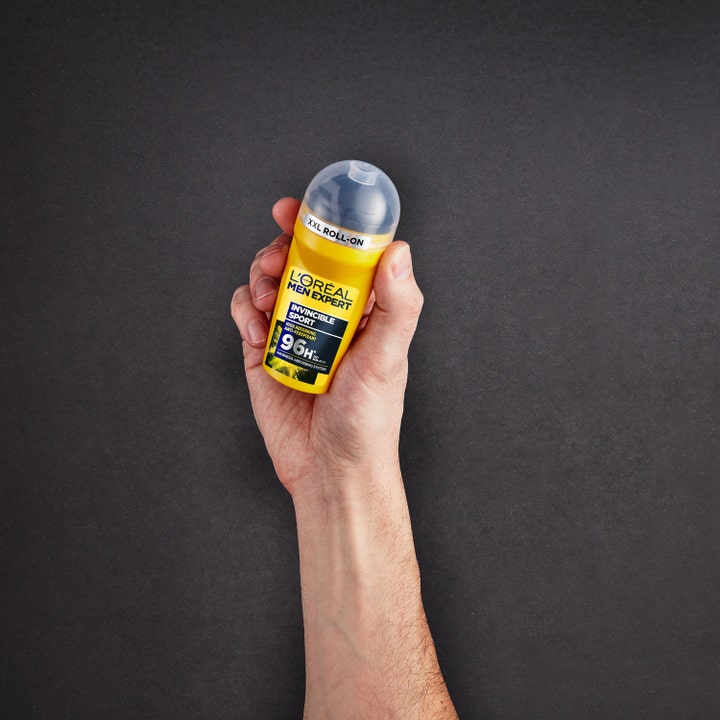 L’Oréal Paris Men Expert Invincible Sport 96H 50 ml herrdeodorant i gul roll-on-flaske som holdes i en hånd.