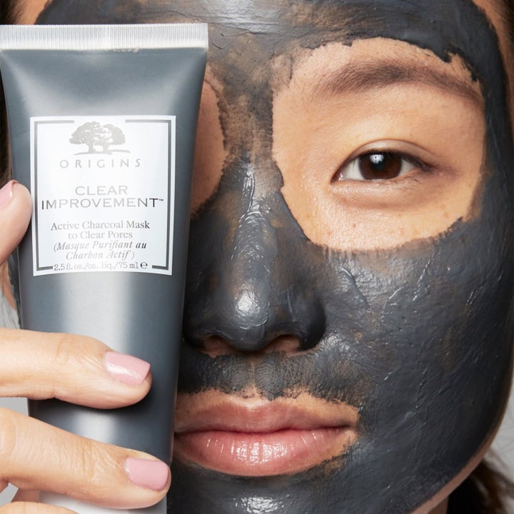 Origins Clear Improvement Active Charcoal Mask 75 ml ansiktsmaske som renser porer påført i ansiktet ved siden av grå tube.