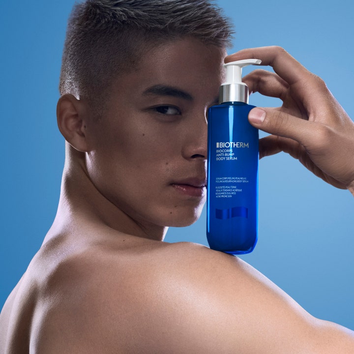 Biotherm Biocorps Body Serum 200 ml eksfolierende kroppsserum i blå pumpeflaske holdt av en mann