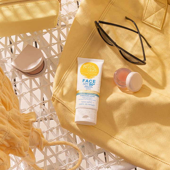 Bondi Sands SPF50+ Hydrating Tinted Face Lotion 75 ml farget solkrem i tube ved en gul strandveske og solbriller