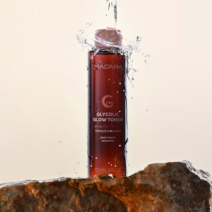 MÁDARA Glycolic Glow Toner 150 ml eksfolierende toner i brun flaske på en stein med vannsprut som gir huden ny glød