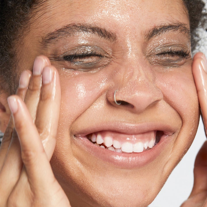 Clinique Take The Day Off Cleansing Balm 125 ml fjerner sminke vist på en smilende kvinne som masserer ansiktet.