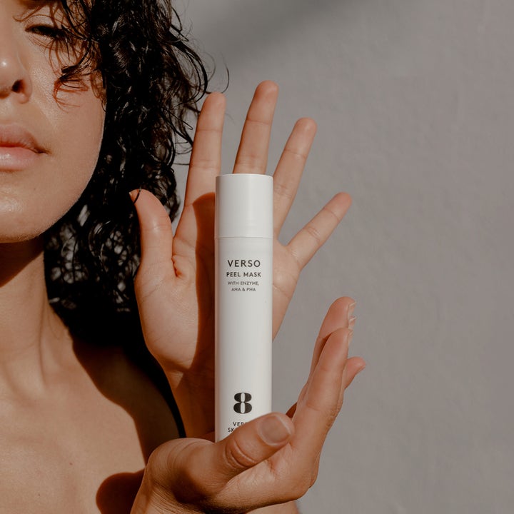 Verso N°8 Peel Mask 50 ml eksfolierende ansiktsmaske gir glød i hvit beholder som holdes av en person.