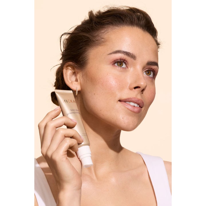 Hickap Honey Glow Priming Moisturizer 50 ml fuktighetsgivende dagkrem i gulltube holdt av kvinne med strålende hud