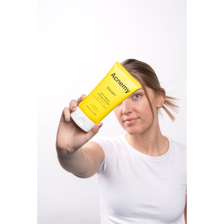 Niche Beauty Lab Acnemy Zitcalm Cleansing Gel 150 ml beroligende ansiktsrens i gul tube holdt av en kvinne