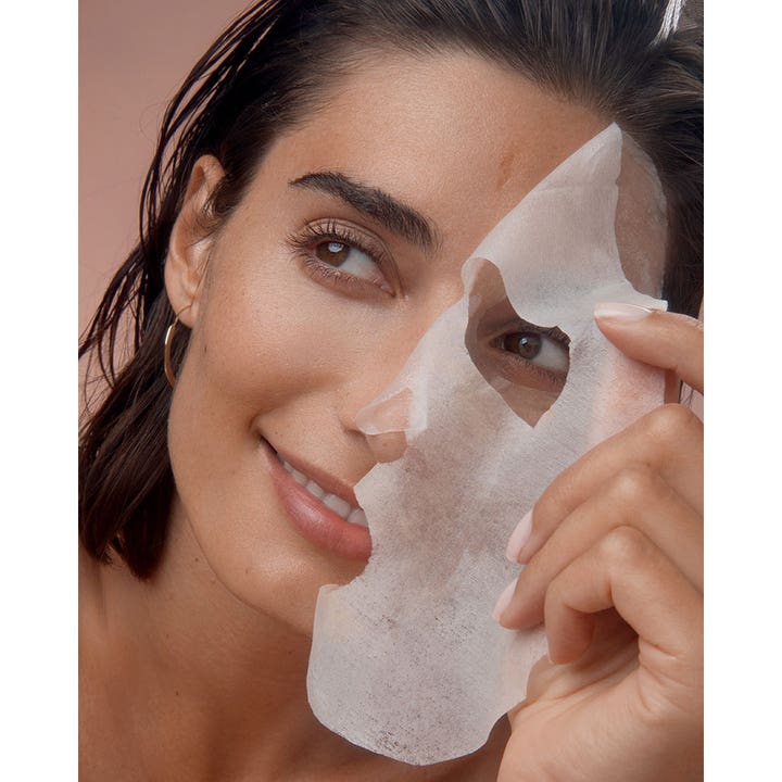 NIVEA Q10 Energy Sheet Mask 1 stk energigivende ansiktsmaske som en kvinne holder opp foran sitt smilende ansikt