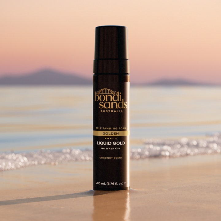 Bondi Sands Liquid Gold Self Tanning Foam 200 ml selvbruning i svart flaske på en strand ved solnedgang.