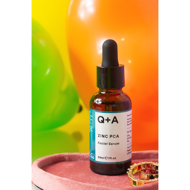 Q+A Zinc PCA Facial Serum 30 ml minimerer porer i en brun glassflaske med pipette foran fargerike ballonger