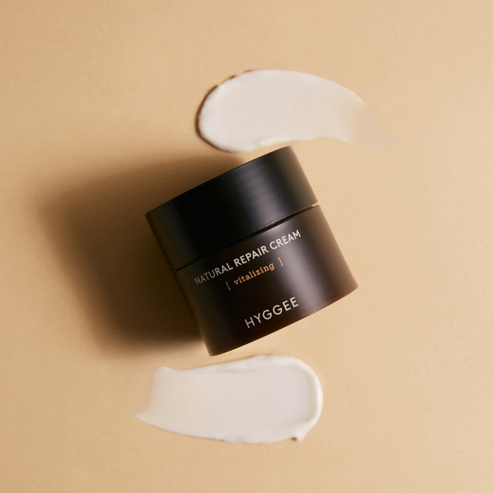 Hyggee Natural Repair Cream 50 ml vitaliserende ansiktskrem i mørkebrun krukke omgitt av hvit kremtekstur.