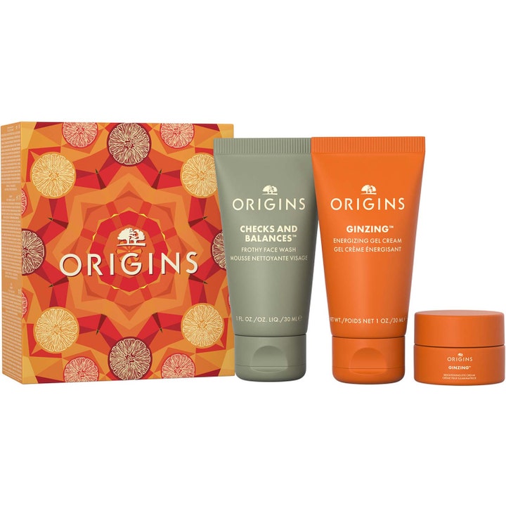 Origins Glow-Boosting Essentials sett med rens og fuktighetskremer i oransje og grønne tuber foran en dekorert eske.