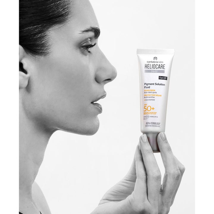 Heliocare Pigment Solution Fluid SPF 50+ 50 ml solkrem mot pigmentflekker i hvit tube holdt av en kvinne.