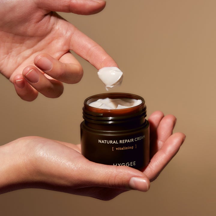 Hyggee Natural Repair Cream 50 ml vitaliserende ansiktskrem i mørkebrun krukke med rik hvit krem på en finger.
