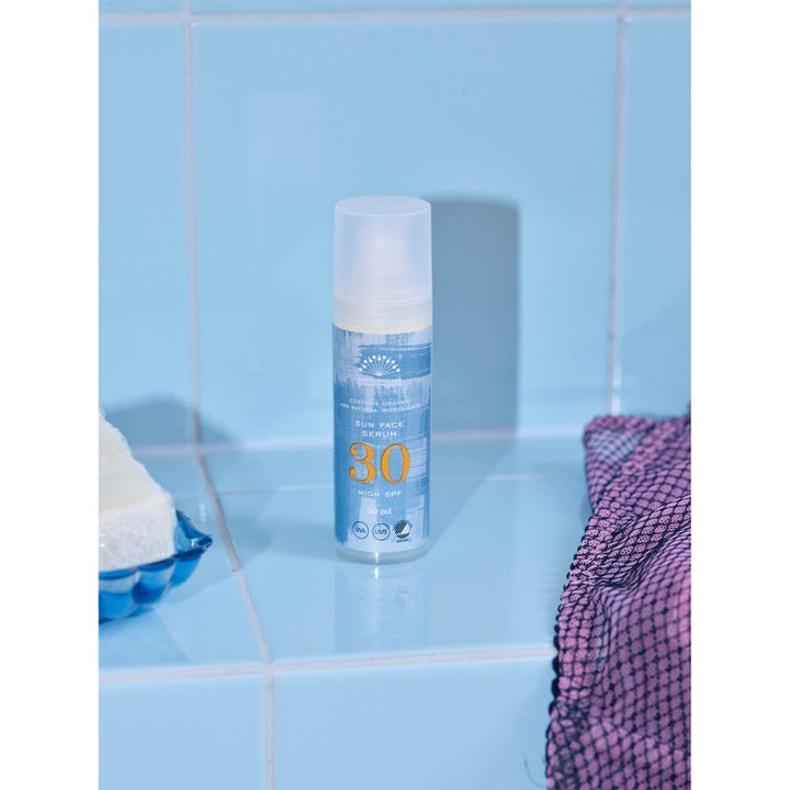 Rudolph Care Sun Face Serum 30 ml beskyttende solkrem ansikt i blå pumpeflaske på lyseblå fliser.