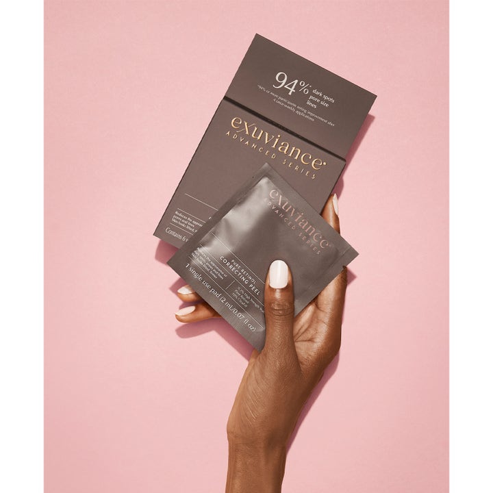 Exuviance Pure Retinol Correcting Peel 6 stk ansiktspeeling mot linjer i grå sachet holdt av en hånd.