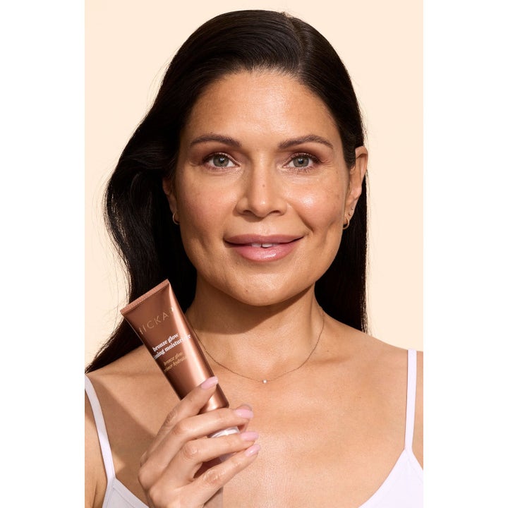 Hickap Bronze Glow Priming Moisturizer gir glødende hud på en kvinne som holder en bronsefarget tube.