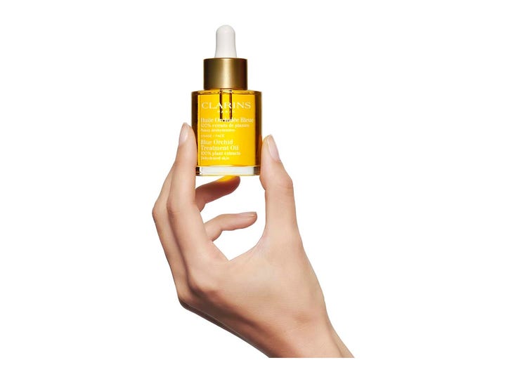 Clarins Blue Orchid Face Treatment Oil 30 ml fuktighetsgivende ansiktsolje i glassflaske med gullkork holdt av en hånd