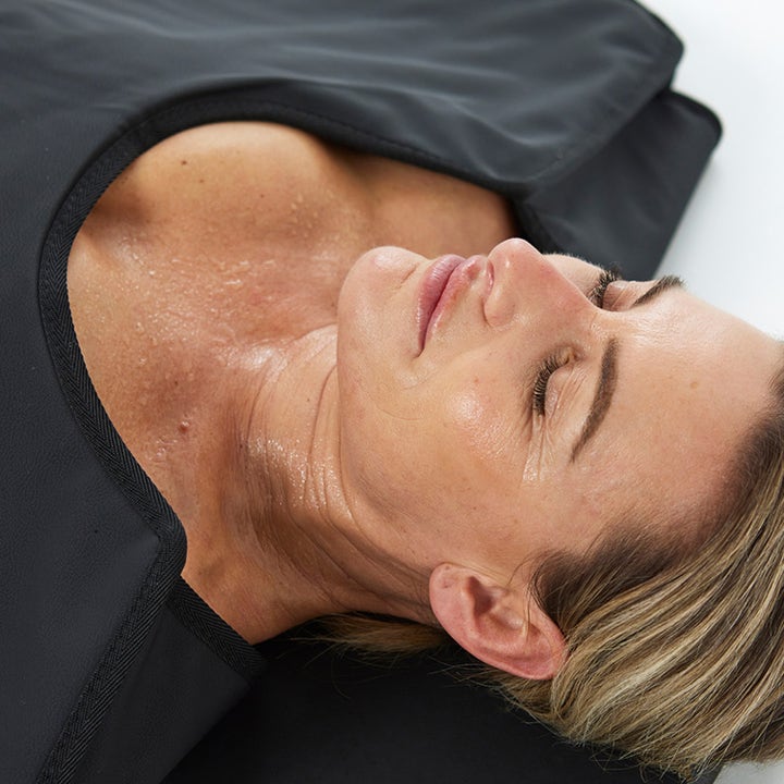 HigherDOSE Infrared Sauna Blanket infrarødt saunateppe gir restitusjon mens kvinne svetter i det svarte teppet.