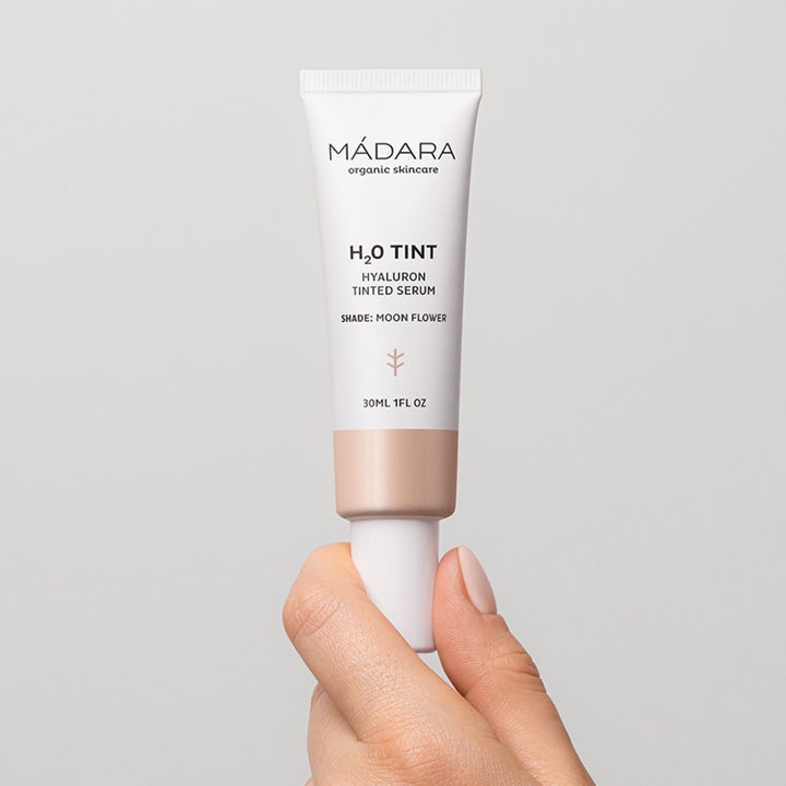MÁDARA H2O Tint Hyaluron Tinted Serum 30 ml fuktighetsgivende serum i hvit tube med beige bunn holdt av en hånd