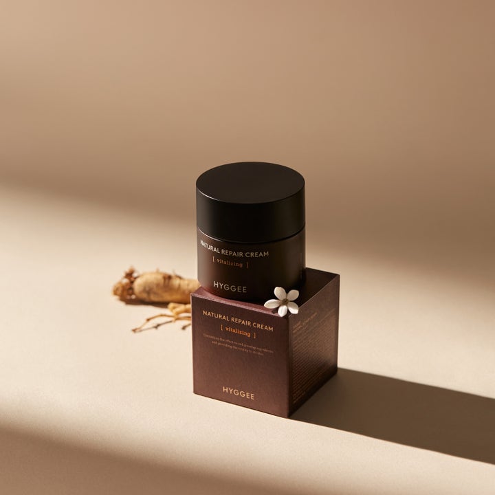 Hyggee Natural Repair Cream 50 ml vitaliserende ansiktskrem i mørkebrun krukke ved siden av hvit blomst og ginsengrot