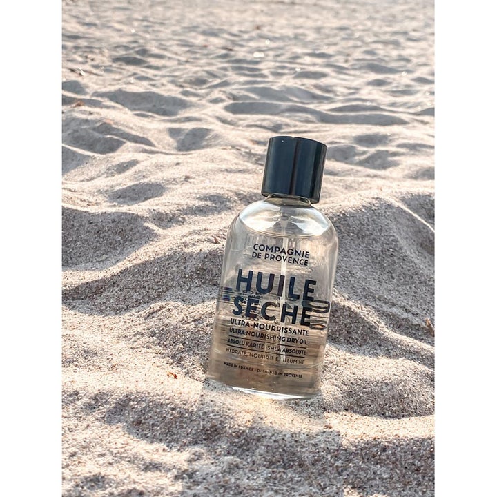 Compagnie de Provence Ultra Nourishing Dry Oil 100 ml nærende hudolje med shea butter i sanden på en strand