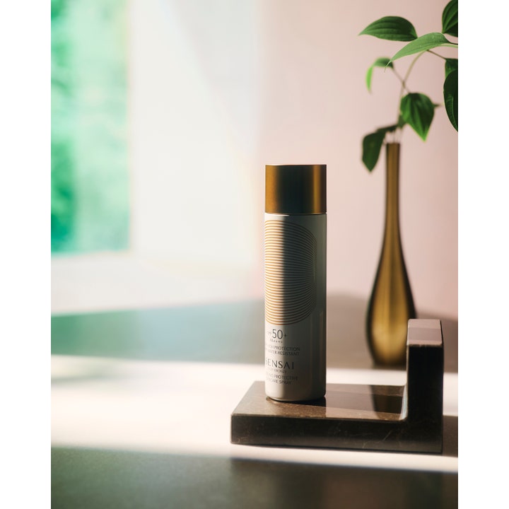 Sensai Silky Bronze Cooling Protective Suncare Spray SPF50 150 ml på mørk marmorplate med en gullvase