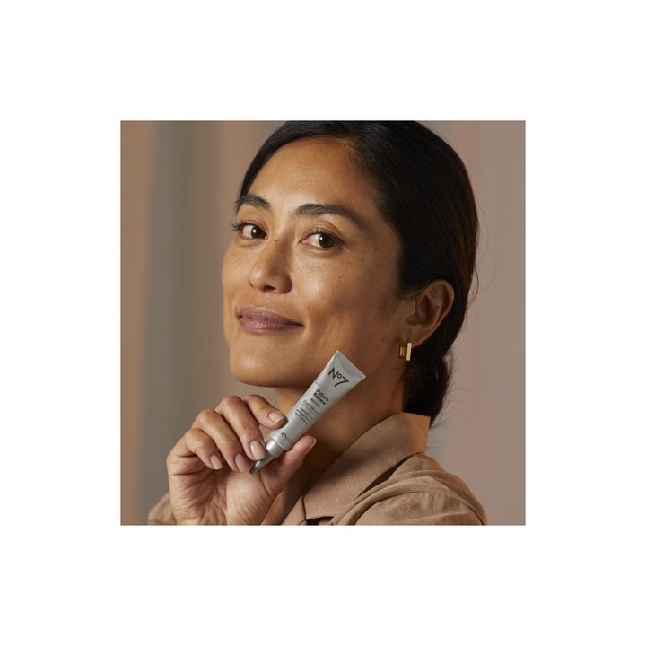 No7 Future Renew Repair Eye Serum 15 ml reparerende øyeserum i grå tube holdt av en smilende kvinne mot kinnet