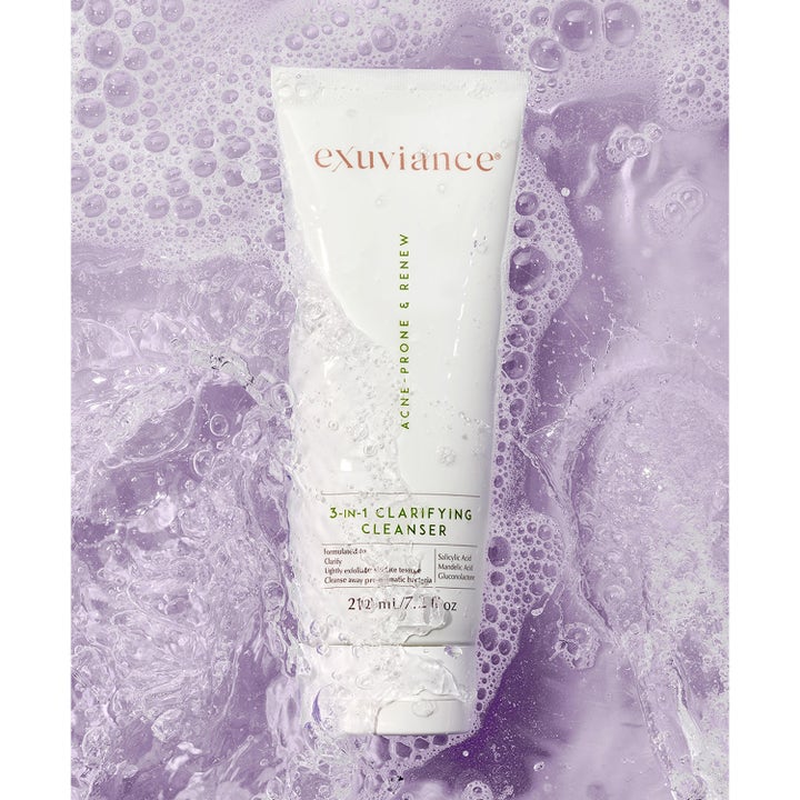 Exuviance 3-in-1 Clarifying Cleanser 212 ml ansiktsrens mot uren hud i hvit tube omgitt av lilla vann og skum