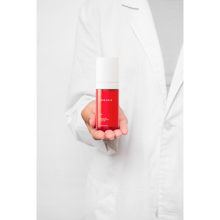 Niche Beauty Lab Theramid Azid 15% Azelaic Acid 30 ml serum i rød flaske holdt av en person i hvit labfrakk.