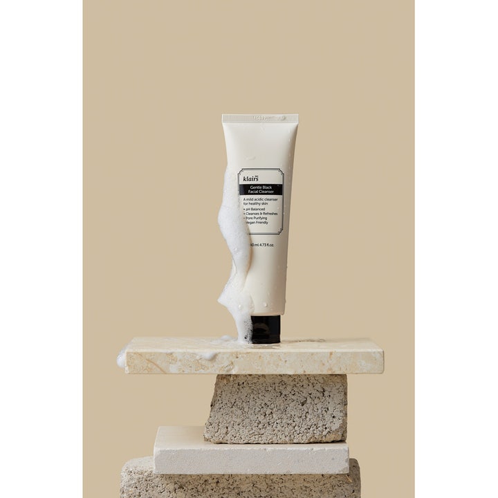 Klairs Gentle Black Facial Cleanser 140 ml fuktighetsgivende ansiktsrens på tube med hvitt skum på beige stein.