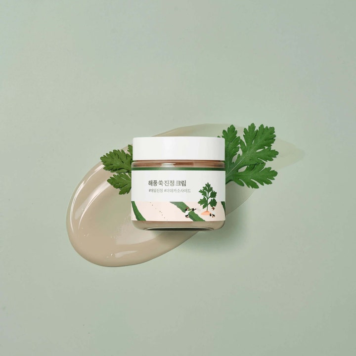 Round Lab Mugwort Calming Cream 80 ml beroligende ansiktskrem i krukke over en myk tekstur og grønne blader.