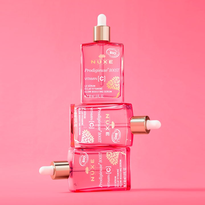 Nuxe Prodigieuse Boost Vitamin C Serum 30 ml gir glød i tre rosa glassflasker stablet mot rosa bakgrunn.