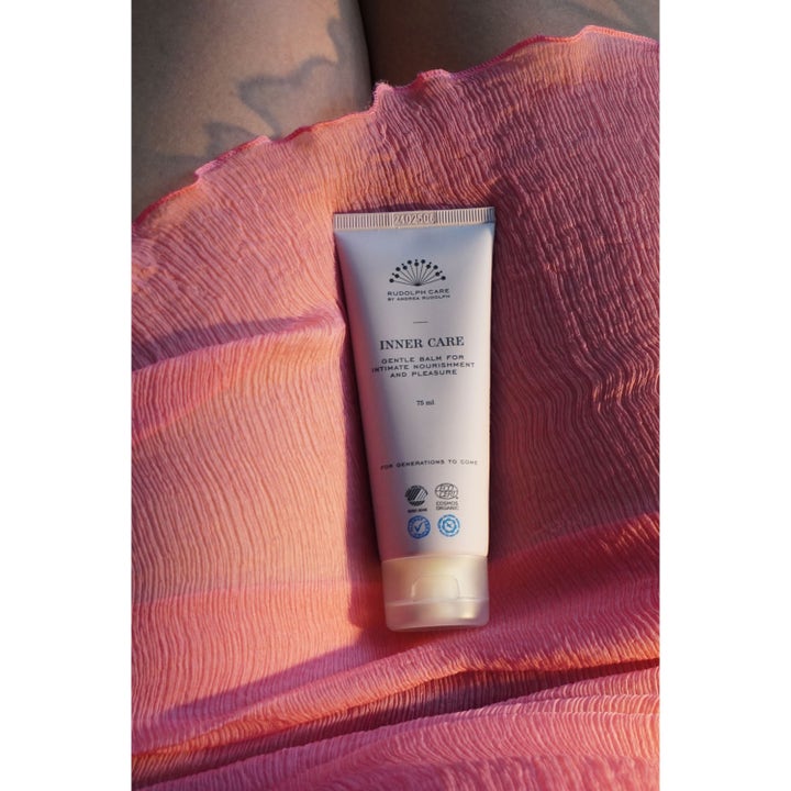 Rudolph Care Inner Care Body Balm 75 ml nærende body balm for intimpleie i lys tube på rosa plissert stoff.