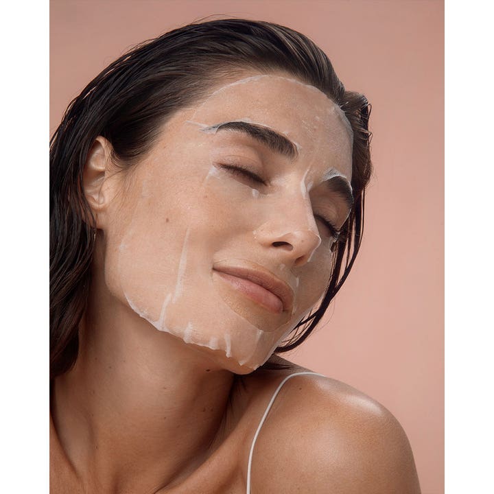 NIVEA Q10 Energy Sheet Mask 1 stk fuktighetsgivende ansiktsmaske påført en kvinne som slapper av mot rosa bakgrunn