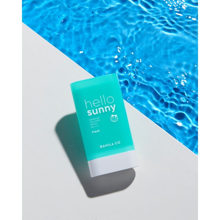 Banila Co Hello Sunny Essence Sun Stick 18,5 g solkrem ansikt i turkis hylse ved et glitrende blått basseng