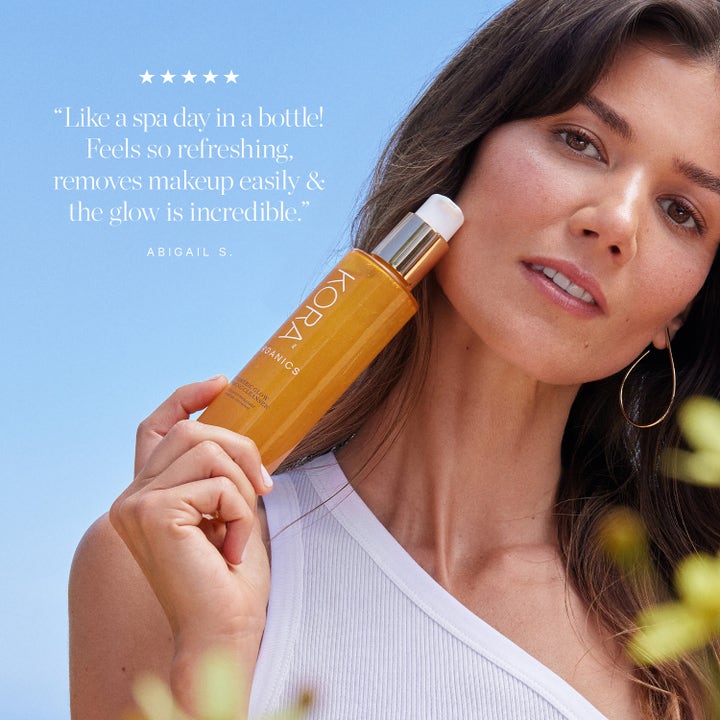KORA Organics Turmeric Glow Foaming Cleanser 150 ml glødgivende ansiktsrens i gyllen flaske holdt av kvinne