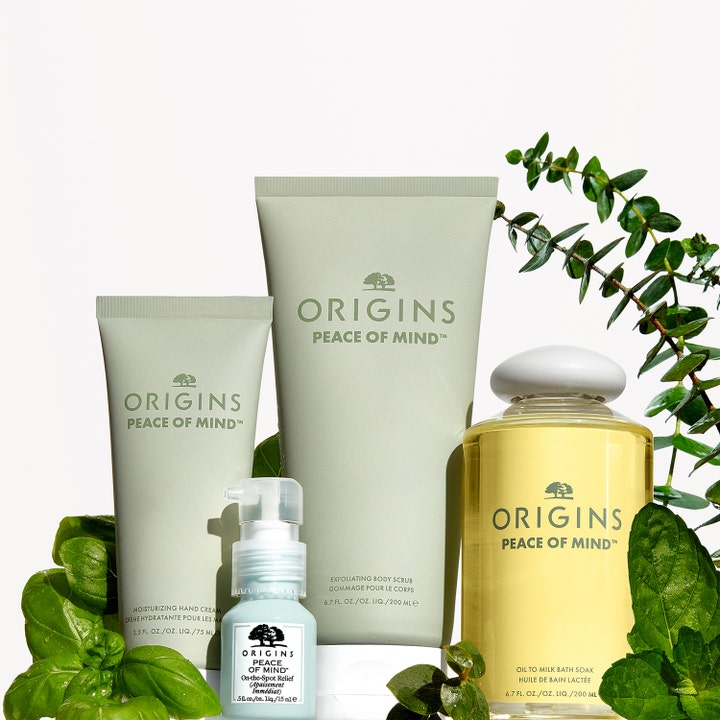 Origins Peace Of Mind Exfoliating Body Scrub 200 ml eksfolierende kroppsskrubb i grønn tube omgitt av friske urter
